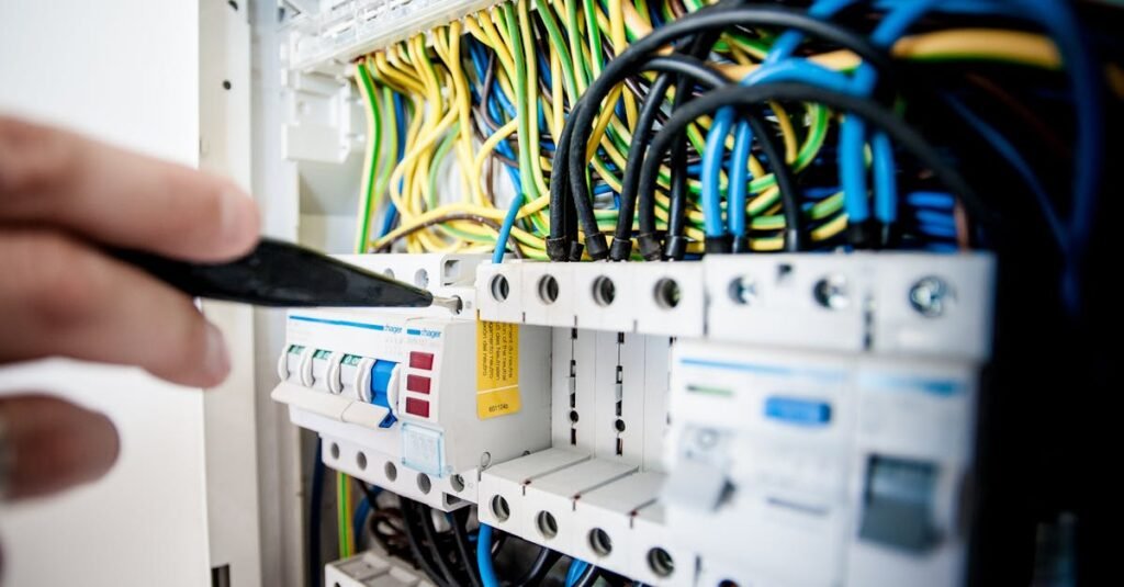 Hand of electrician working on a circuit breaker panel with colorful wires, ensuring safe electrical connections.