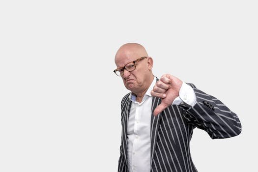 Bald businessman in striped coat giving a thumbs down gesture against a white background.