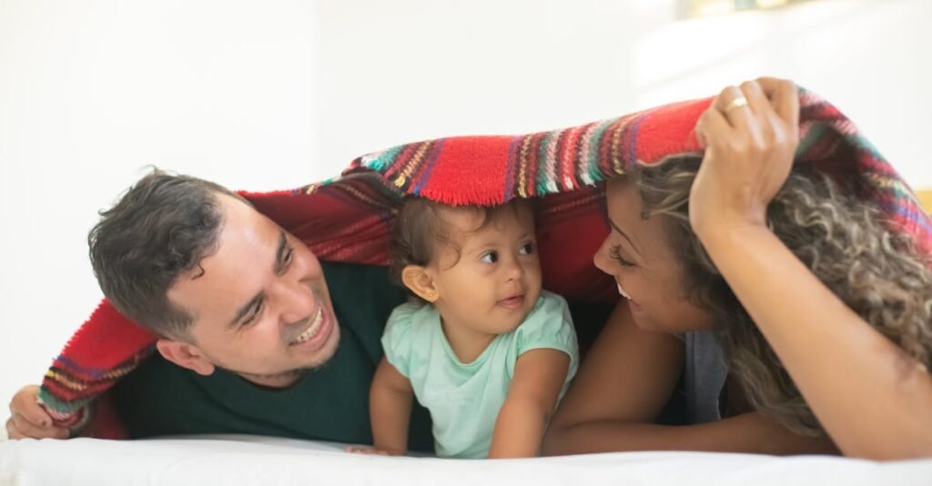 Joyful family of three sharing loving moments under a blanket indoors.