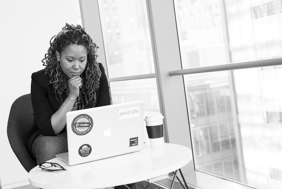 Woman sitting at laptop, focused on remote work. Black and white aesthetic indoors.