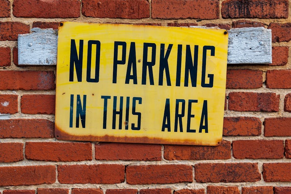 Bright yellow no parking sign attached to a red brick wall.