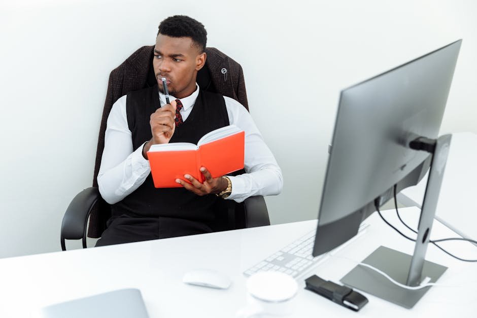 An adult man in a business suit holding a notebook while thinking at his desk.
